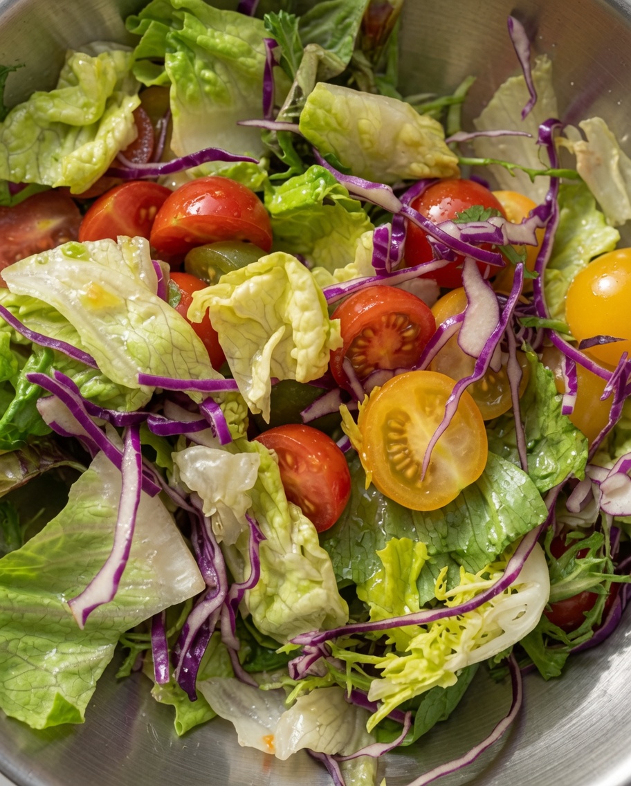 A vibrant mixed salad of green lettuce, purple cabbage, and halved cherry tomatoes tossed together in a metal bowl.