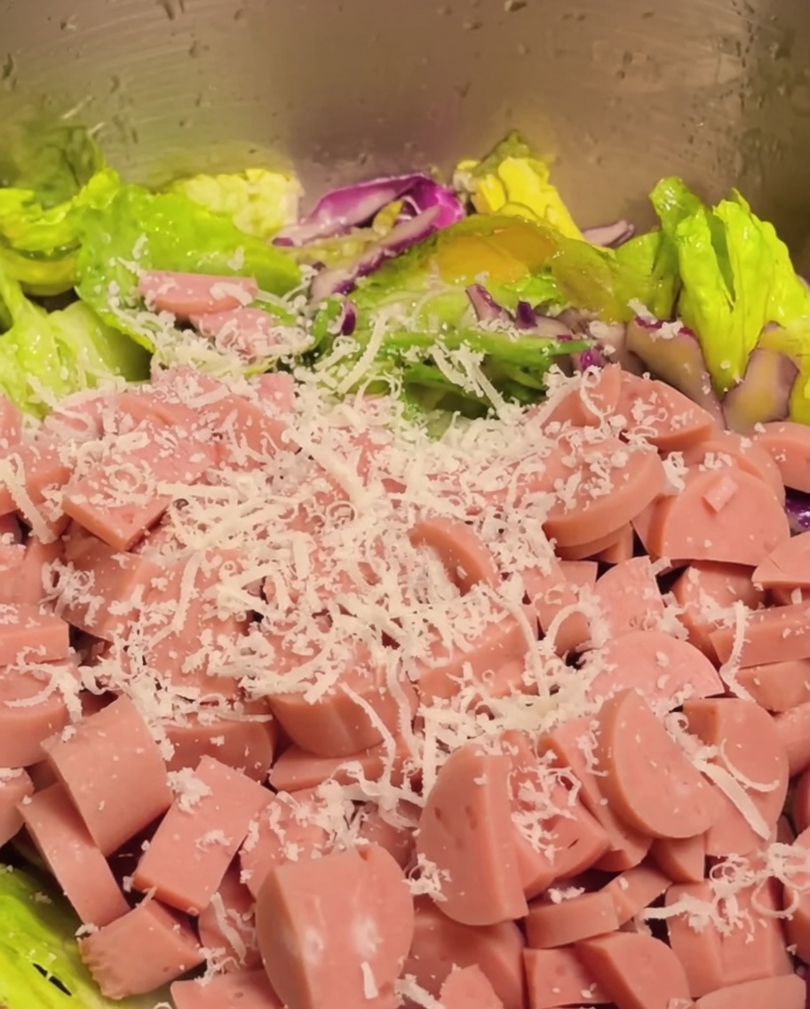 Diced ham and grated Parmesan cheese being added to the vegetable salad mix.