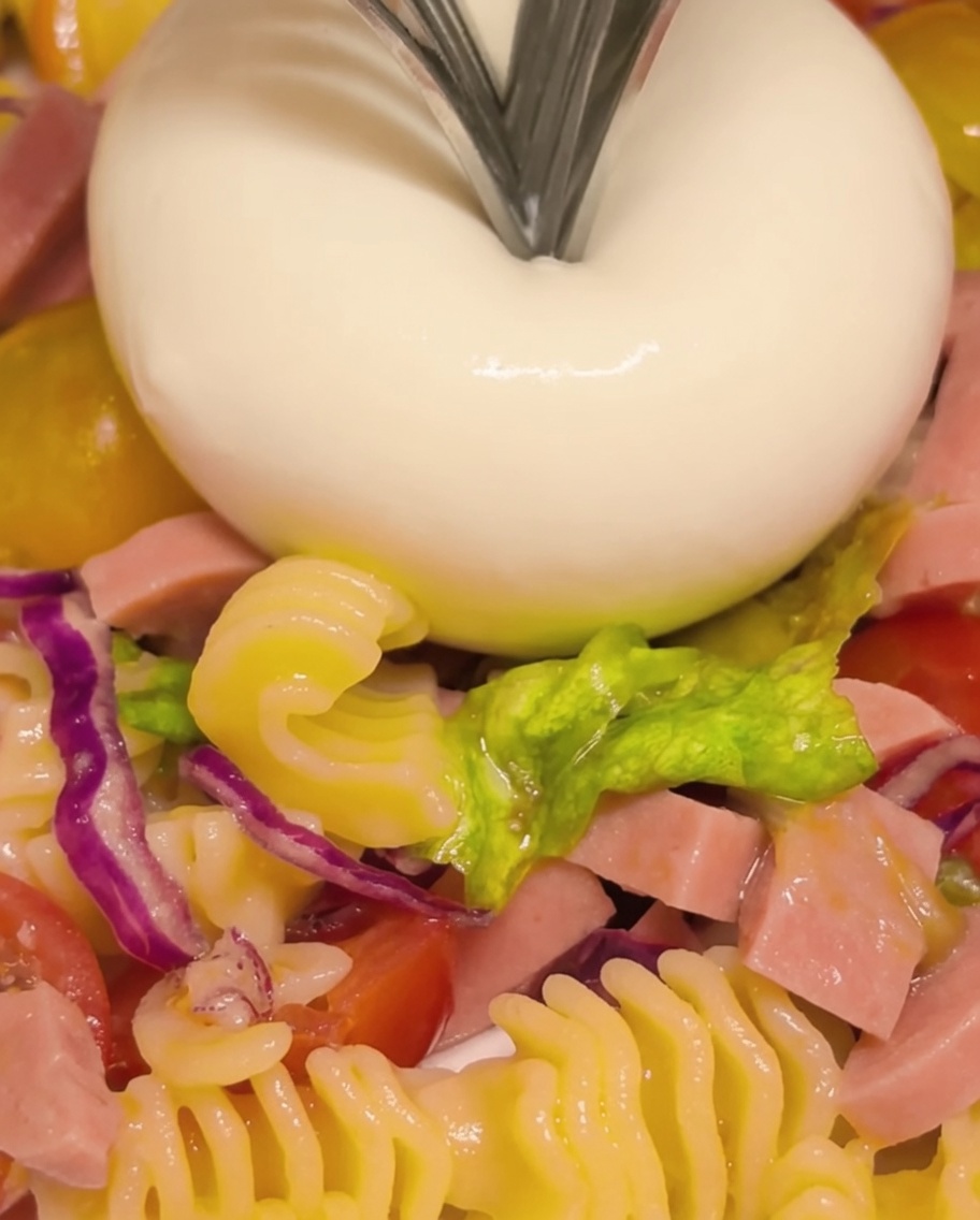 A burrata cheese ball being broken open with a fork to reveal the creamy, flowing center.