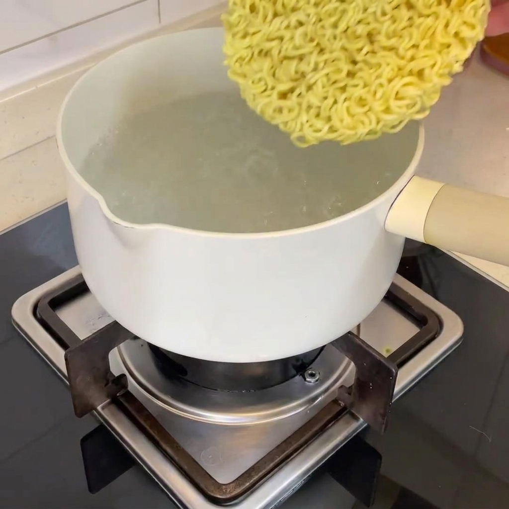 A block of dried ramen noodles being dropped into a pot of boiling water.