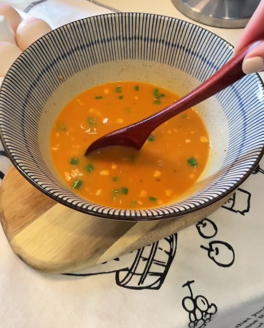 Noodles being lifted with tongs from a pot and placed into a bowl of seasoned broth.