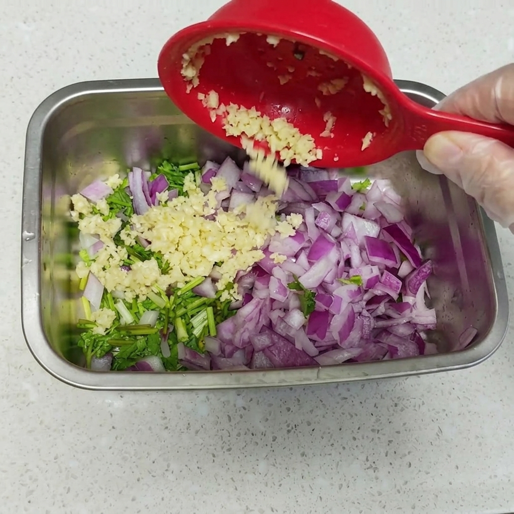A close-up view of peeled, soft-boiled eggs nestled into a bed of chopped cilantro, red onion, and minced garlic inside a metal container.