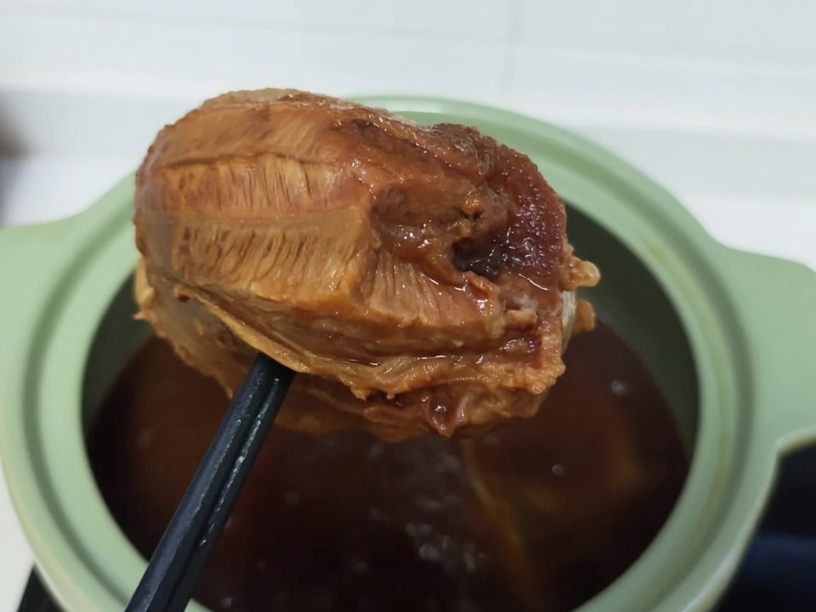 A cooked, browned beef shank being tightly wrapped in clear plastic film.