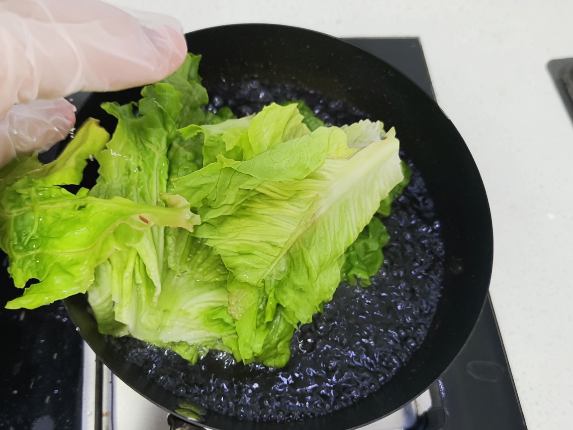 Fresh green leafy vegetables being submerged into a pan of boiling water.