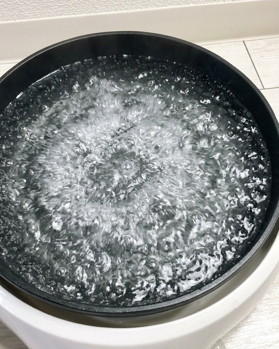 Five raw eggs being lowered into a large pot of actively boiling water.