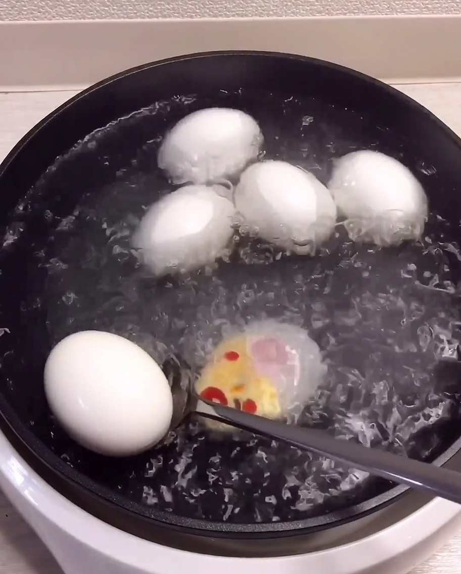 Cooked eggs being scooped out of the pot and moved into a bowl filled with ice and water.