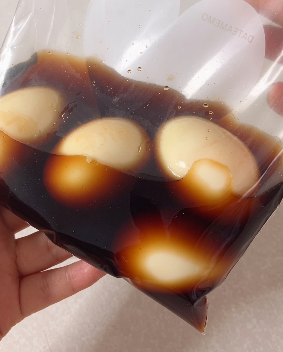 Peeled soft-boiled eggs inside a plastic freezer bag, being covered with the dark soy-based marinade.