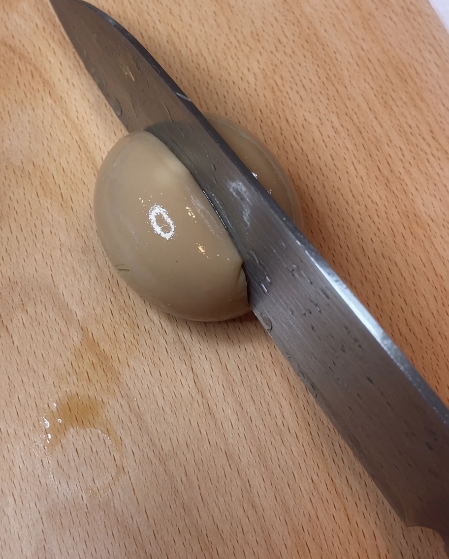 A perfectly halved soy-marinated egg on a cutting board, showcasing a vibrant, jammy yolk.