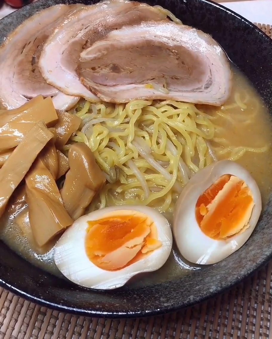An assembled bowl of ramen featuring orderly rows of sliced pork, bamboo shoots, and marinated egg halves.