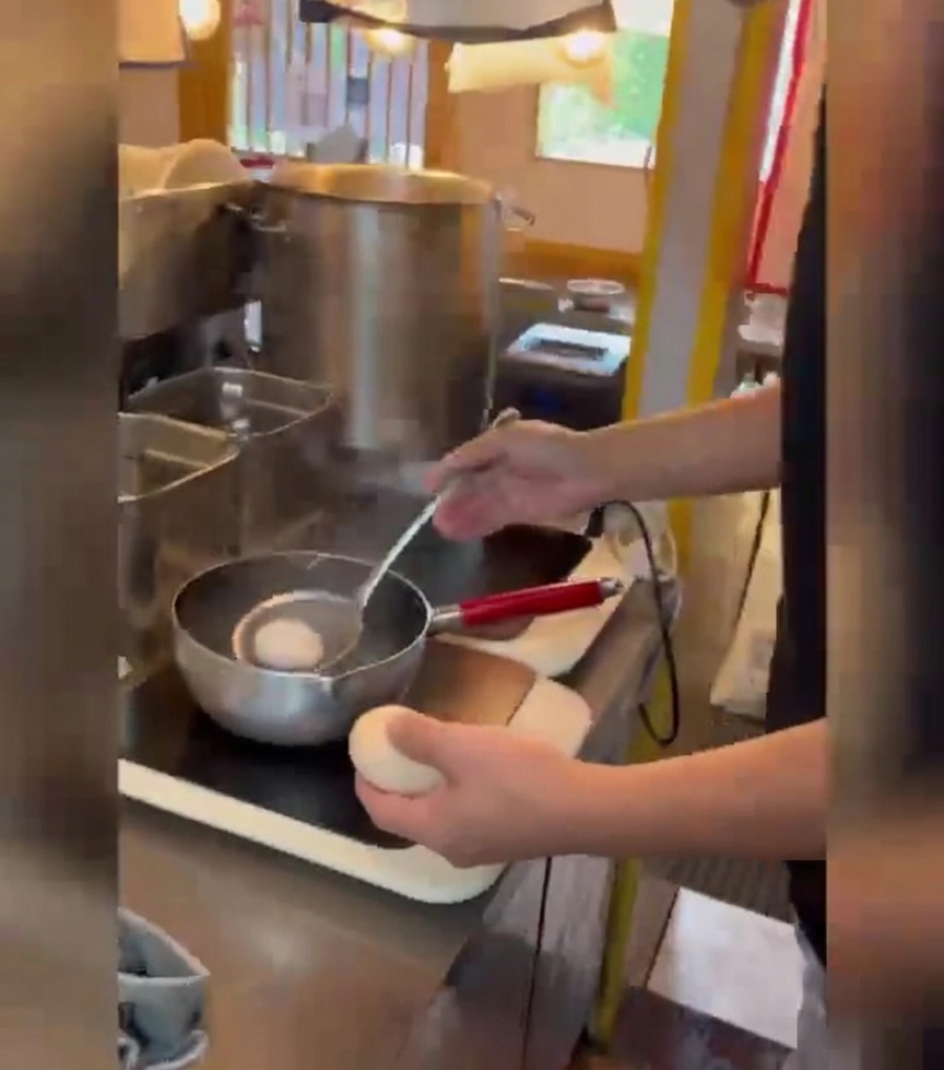 A person using a wire strainer to gently lower white eggs into a pot of boiling water.