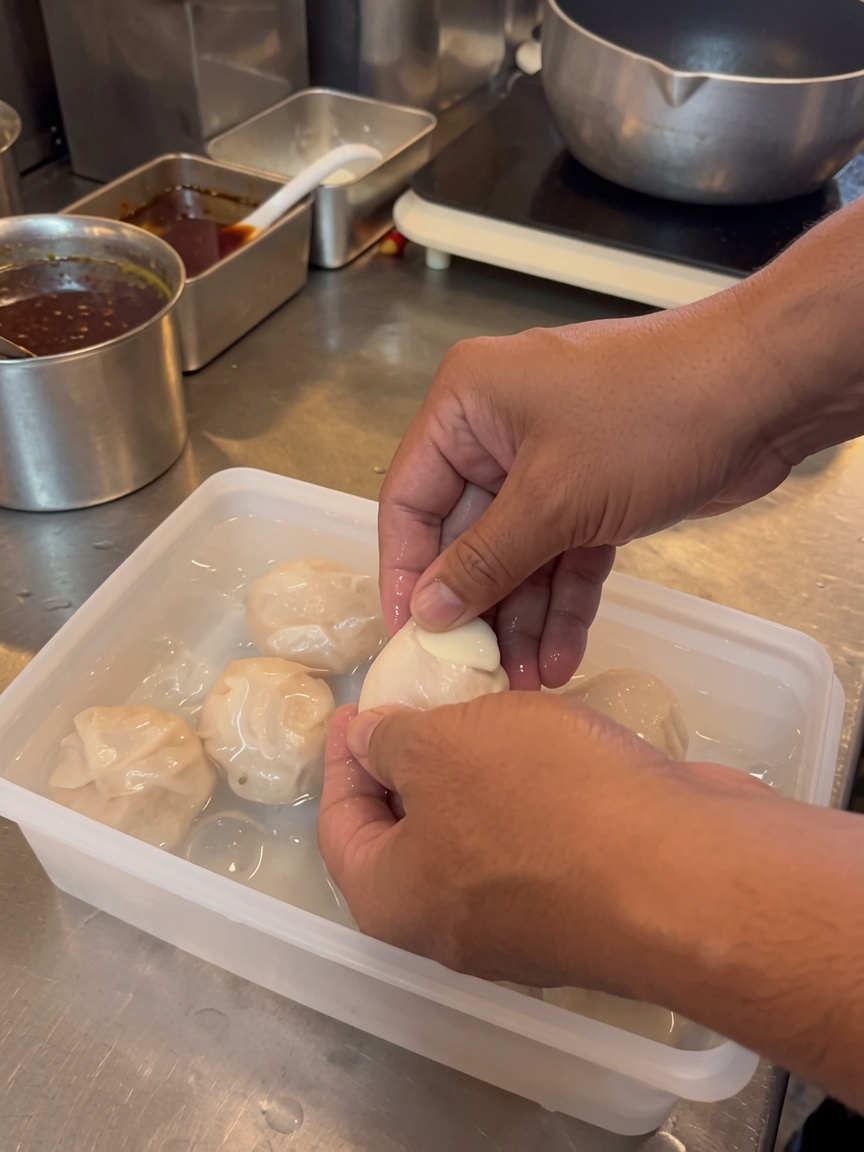 Hands carefully peeling the shell off a soft boiled egg inside a container filled with cold water.
