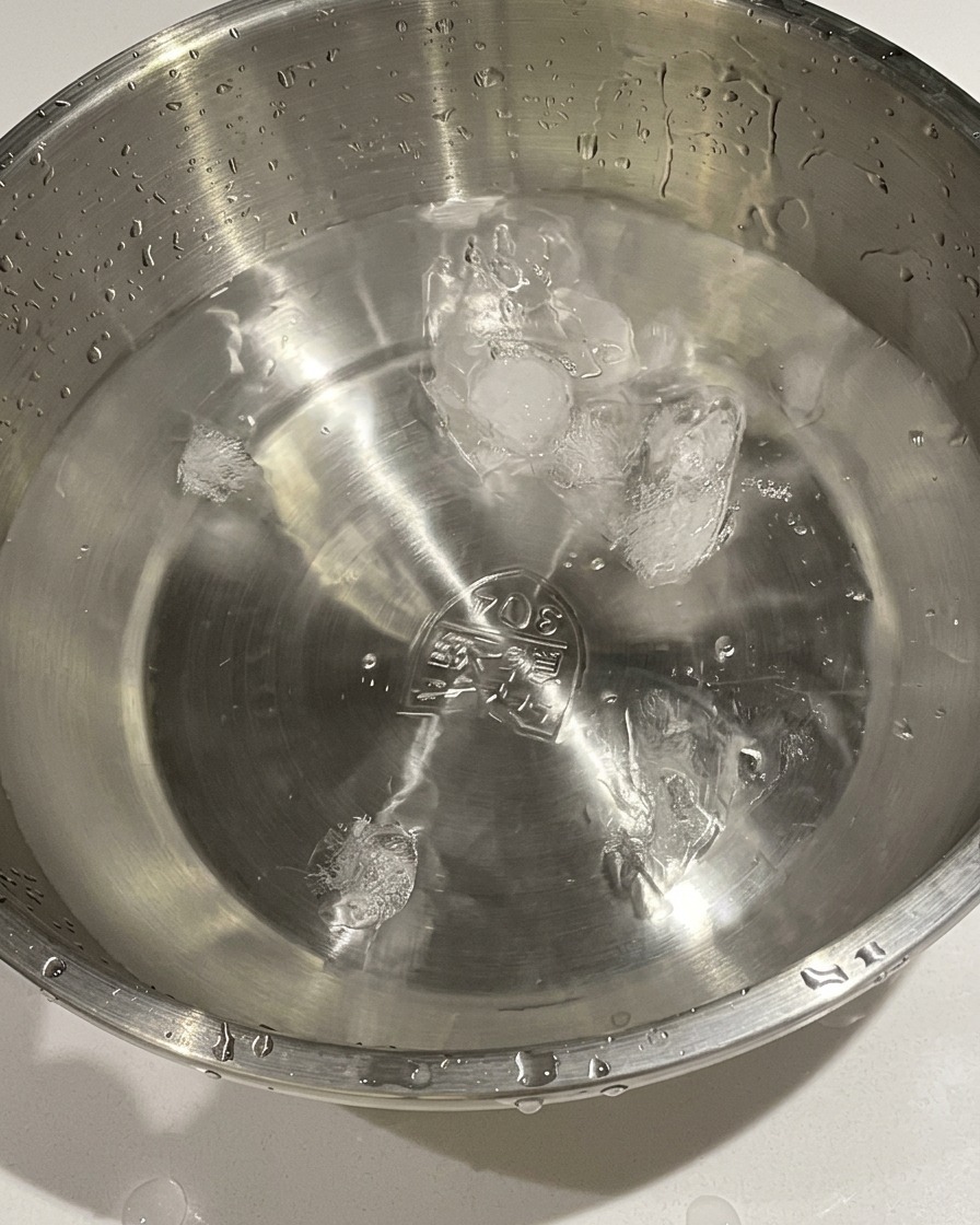 Cooked eggs being transferred from a pot into a metal bowl containing cold water and ice cubes.