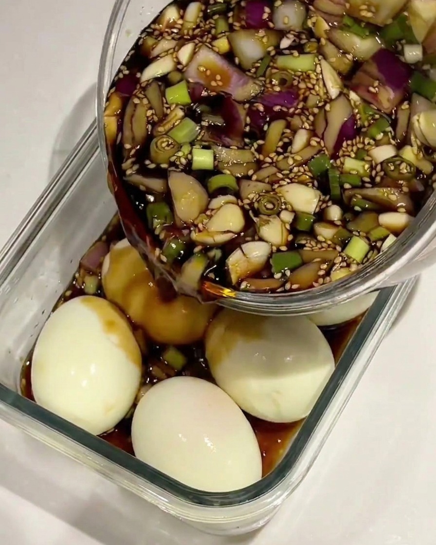 Soy sauce marinade being poured over peeled boiled eggs in a glass container.