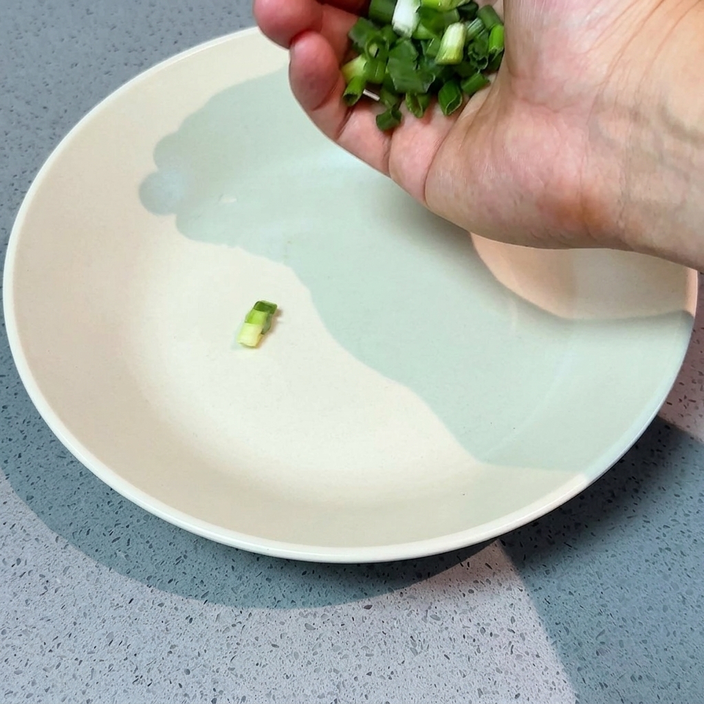 A hand sprinkling freshly chopped green scallions into a large, shallow white serving bowl.