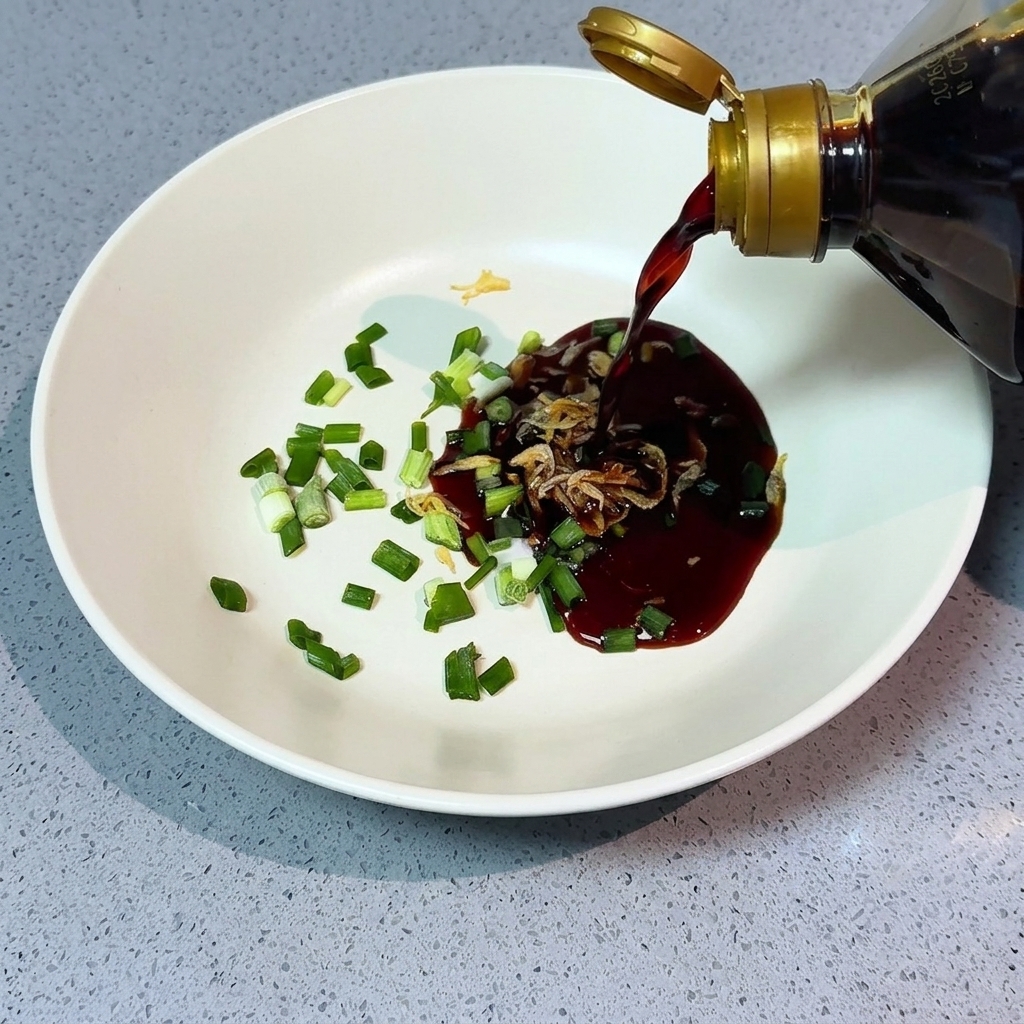 Pouring dark soy sauce from a bottle into a bowl already containing scallions, dried shrimp, and a pool of light soy sauce.