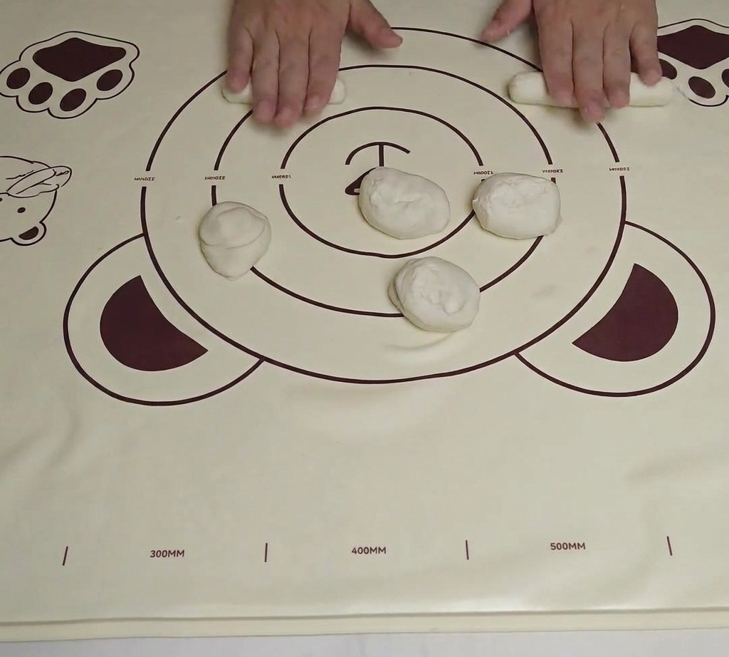 A piece of dough shaped into a short, thick cylinder on a silicone rolling mat.