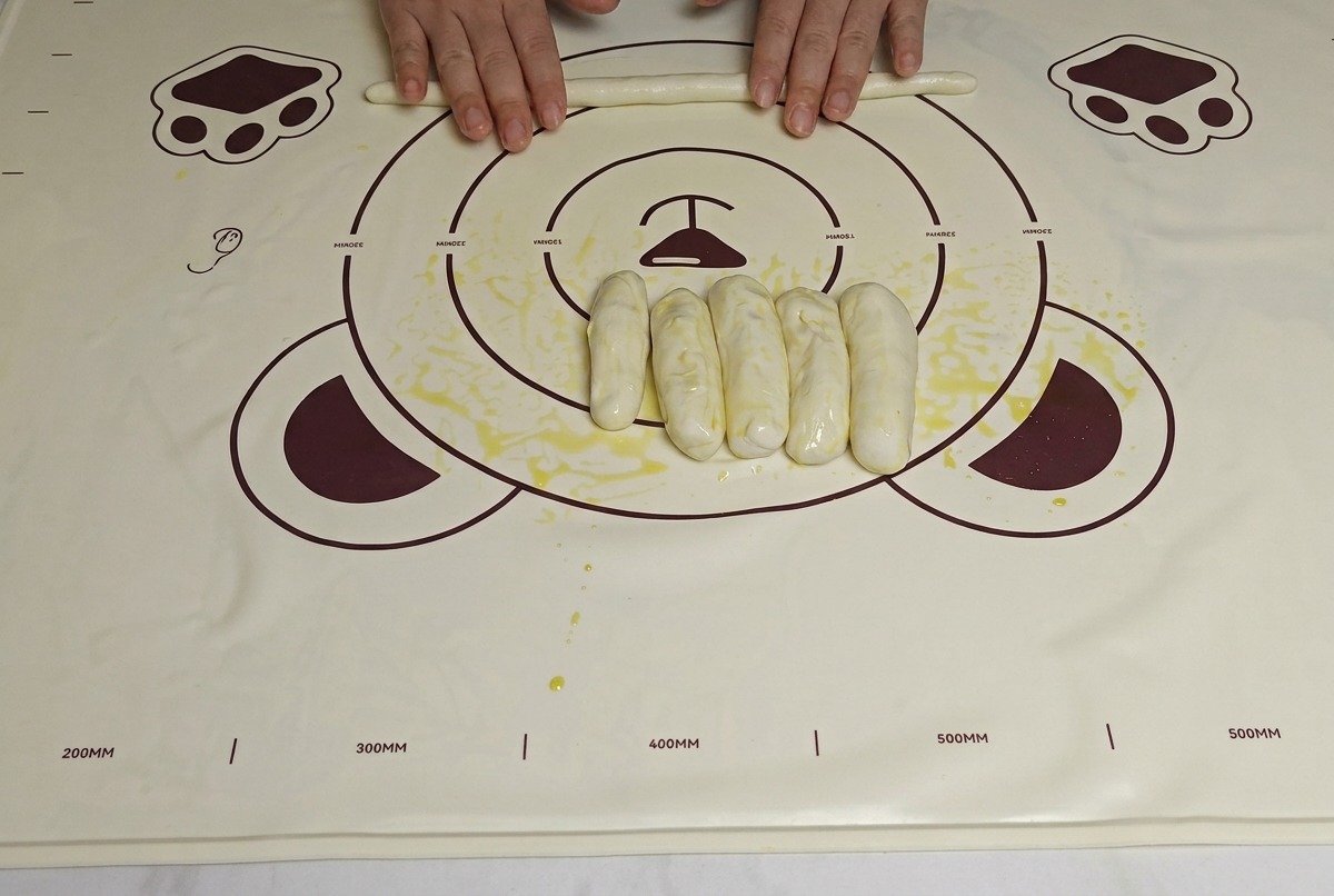 Hands rolling out oiled dough strips on a mat, making them longer and thinner.