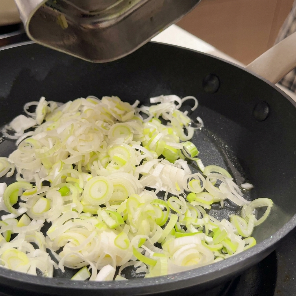 Sliced green onions and minced garlic sizzling in cooking oil in a dark non-stick pan.