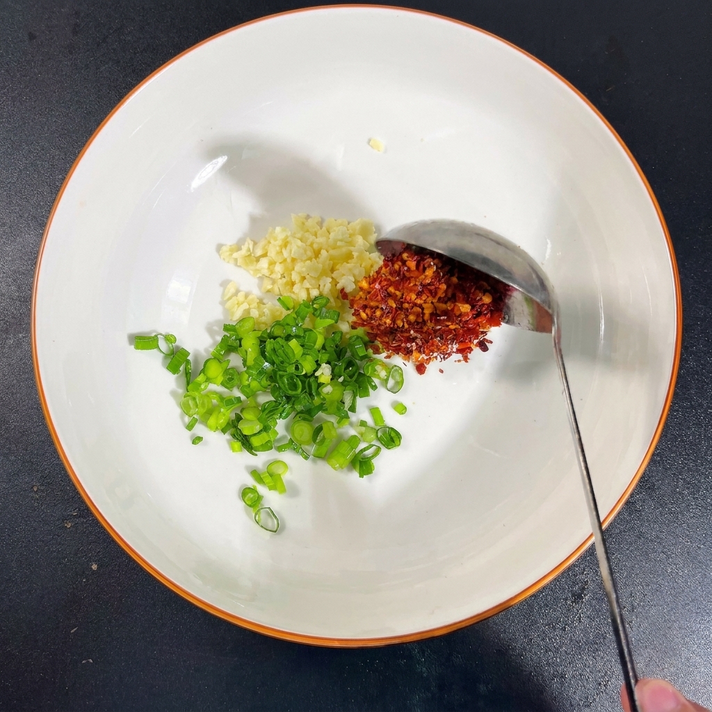 A bowl with garlic, scallions, and mounds of salt, MSG, chili flakes, and a splash of soy sauce.
