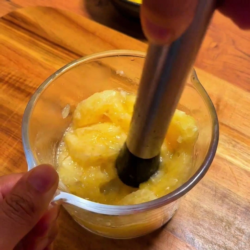 A metal citrus press extracting fresh, vibrant yellow yuzu juice from fruit segments into a glass measuring cup.
