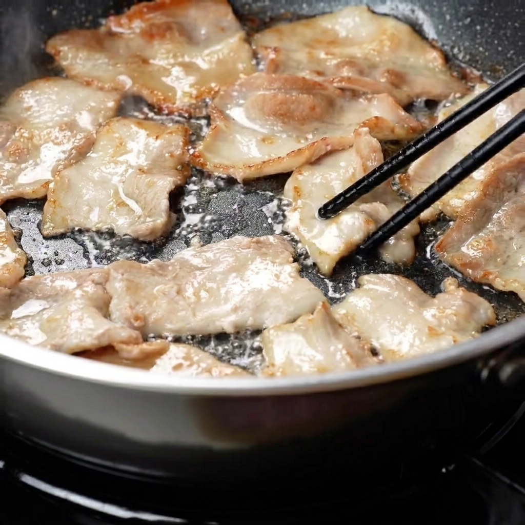 Pork belly slices being flipped in a frying pan to reveal a golden-brown sear.