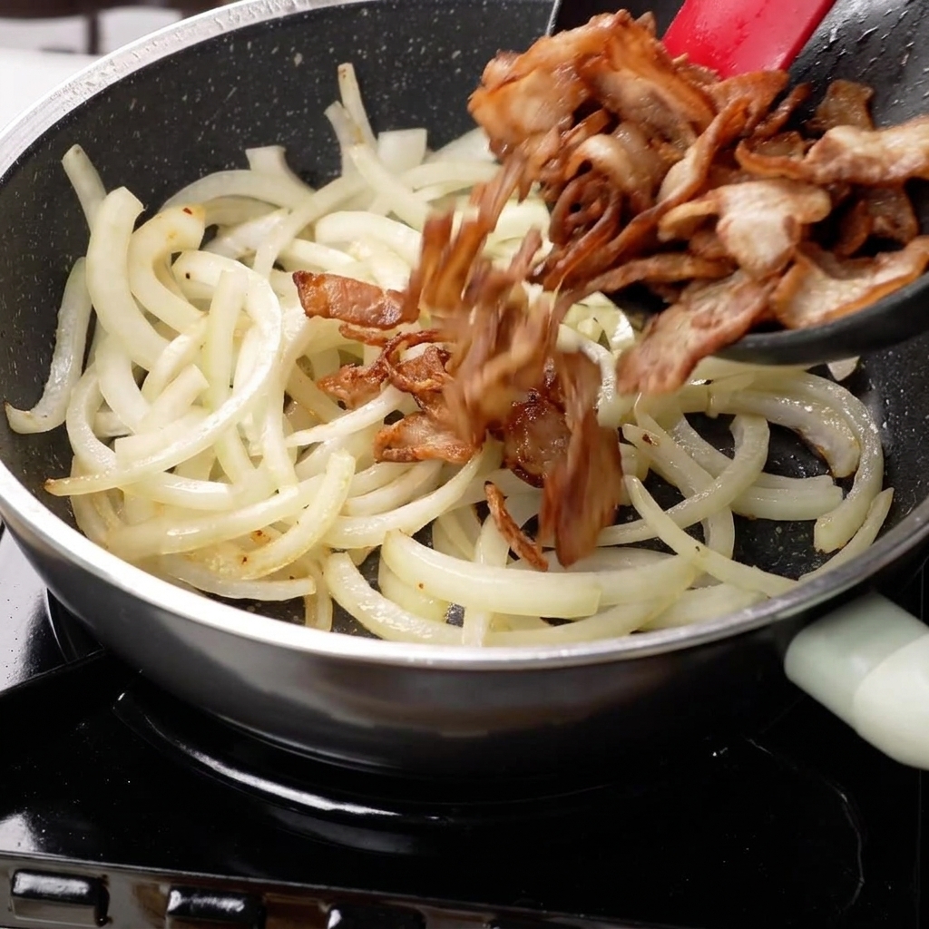 Sautéed onions and seared pork belly being tossed together in a pan.