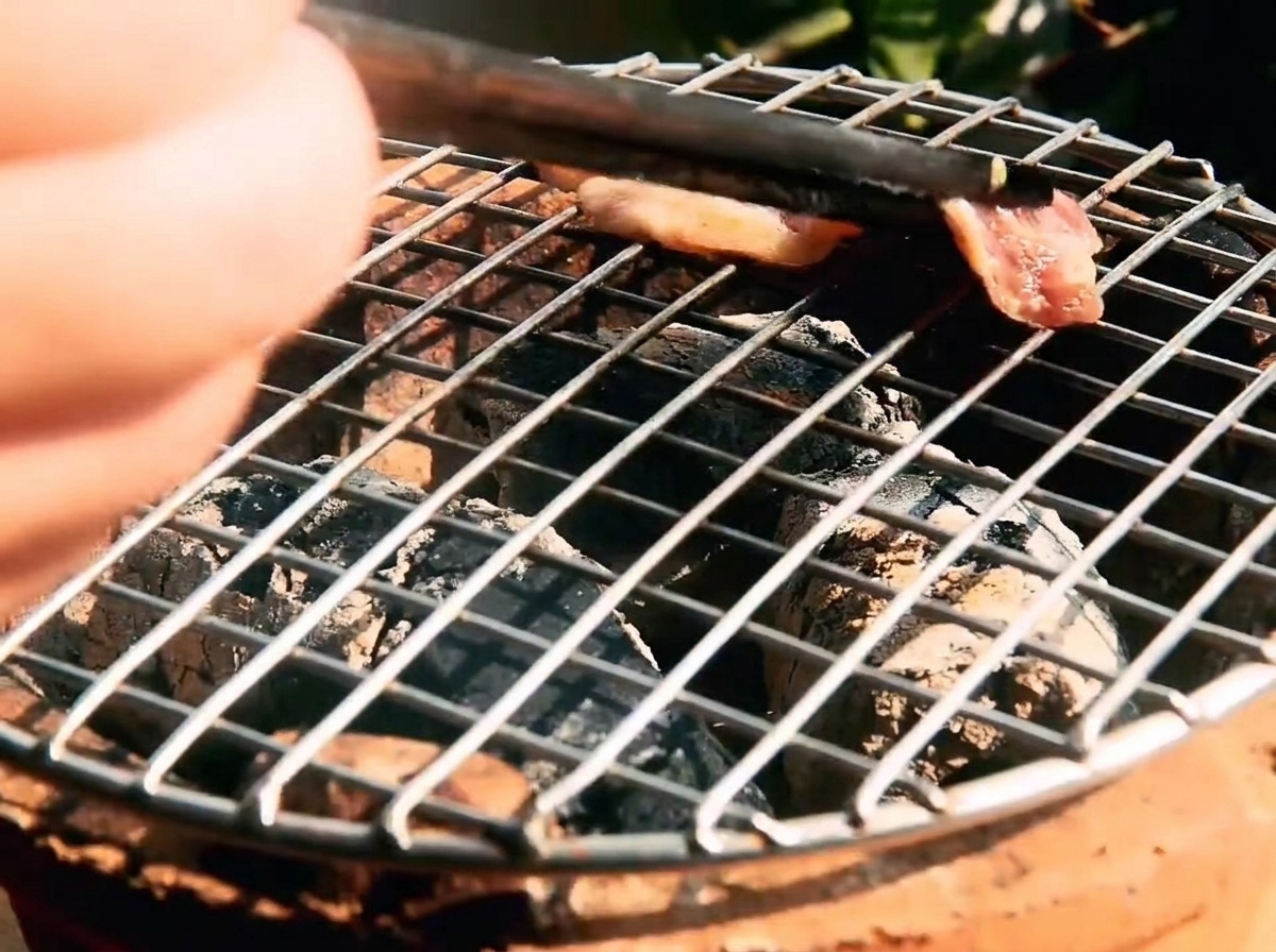 Strips of marinated beef cooking on a hot grill grate with visible glowing coals underneath.