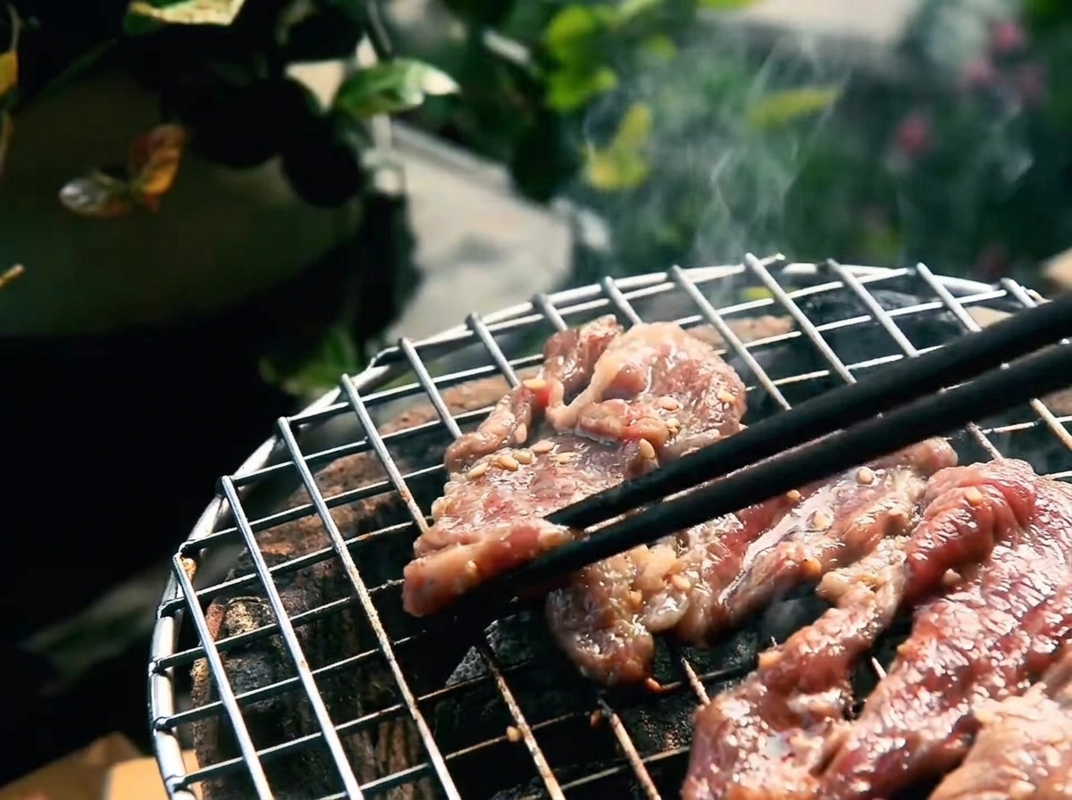 Marinated beef strips grilling on hot coals with visible browning edges and rendered fat.