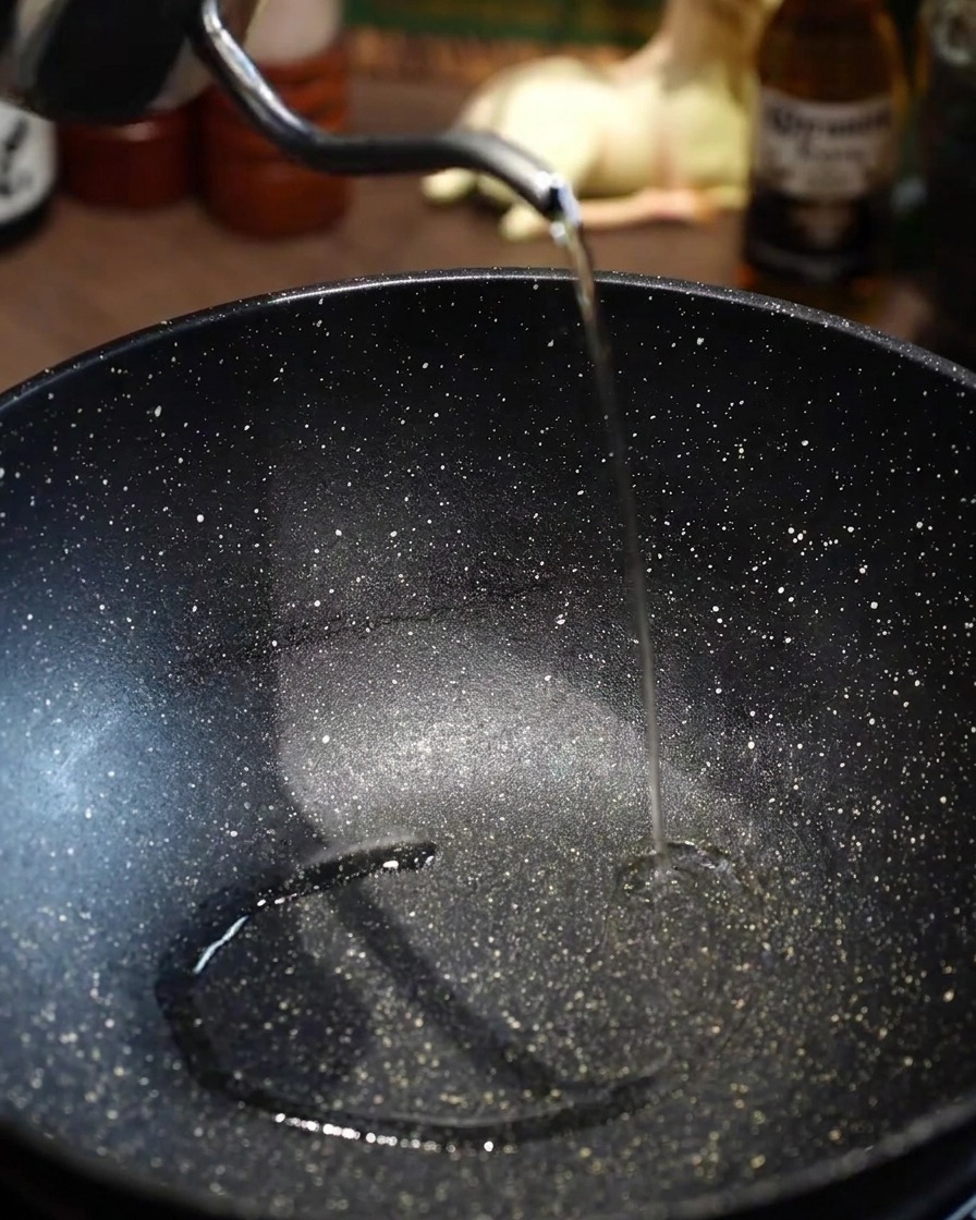 Cooking oil being poured into a preheated, empty black pan.