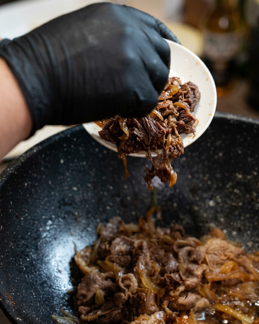 The beef and onion mixture being layered atop a bed of fluffy white rice in a serving bowl.
