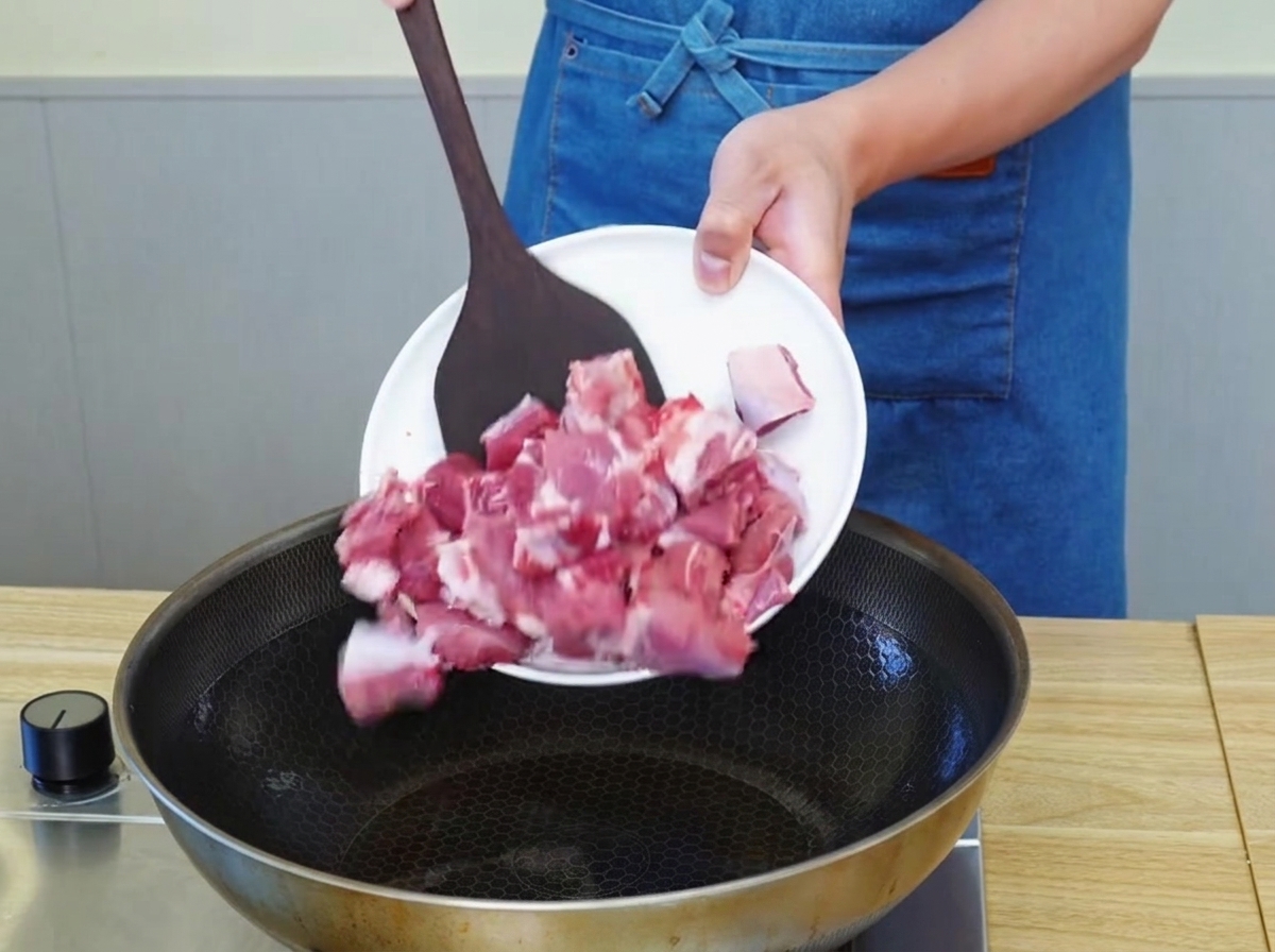 Beef chunks browning in a pan with hot oil, developing a golden-brown crust.