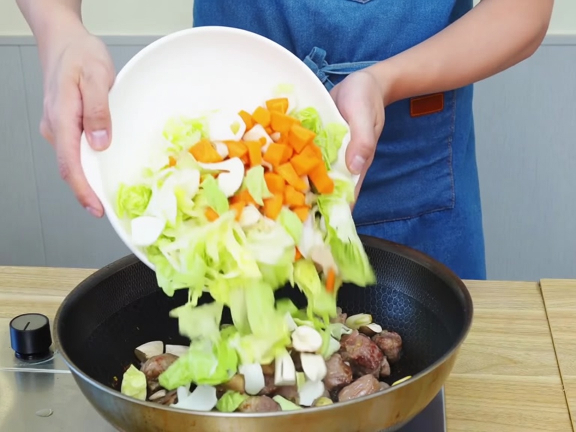 Chopped vegetables and beef pieces being tossed and stir-fried together in a large pan.