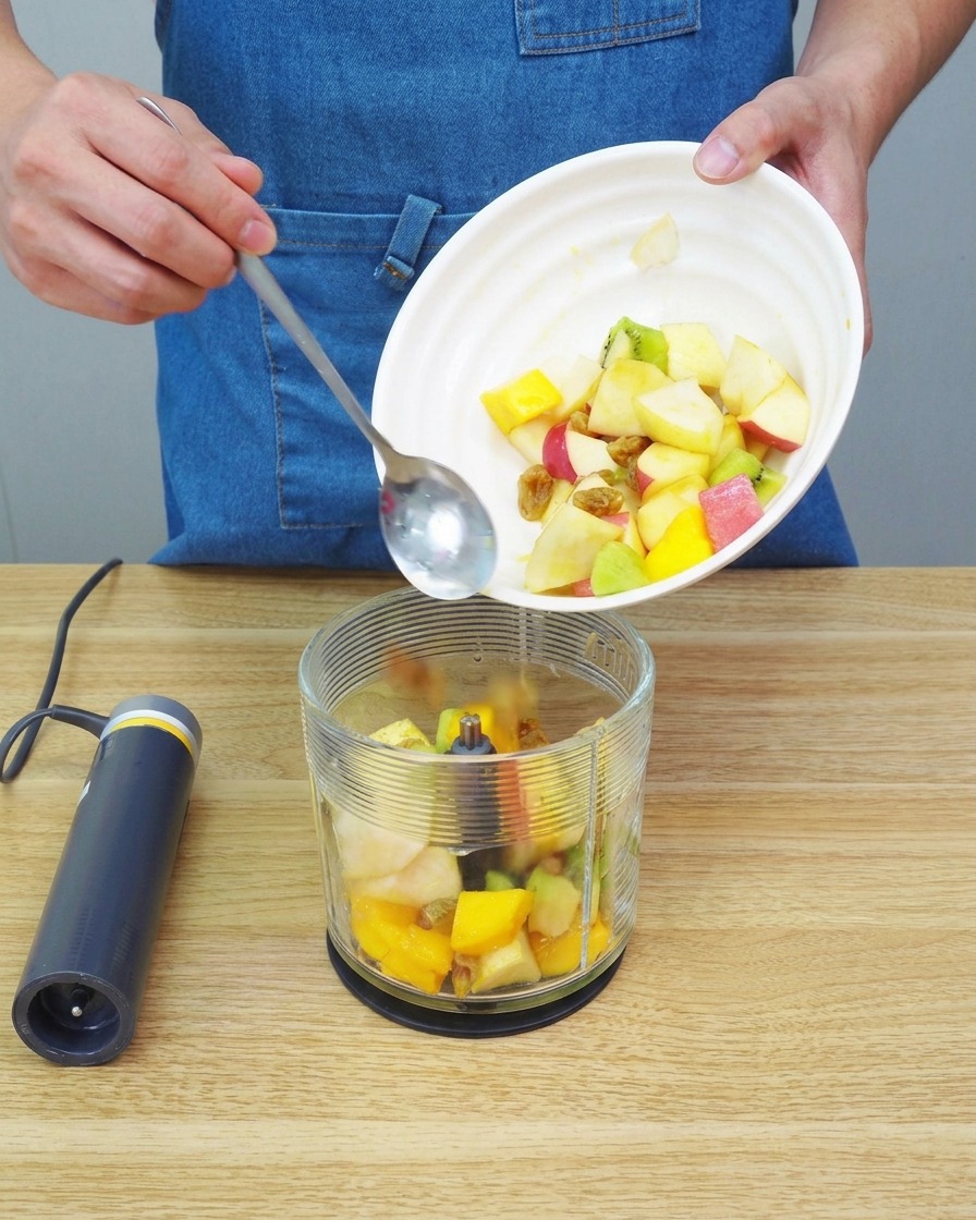 A close-up of fruit pieces being processed into a smooth, thick puree inside a blender container.