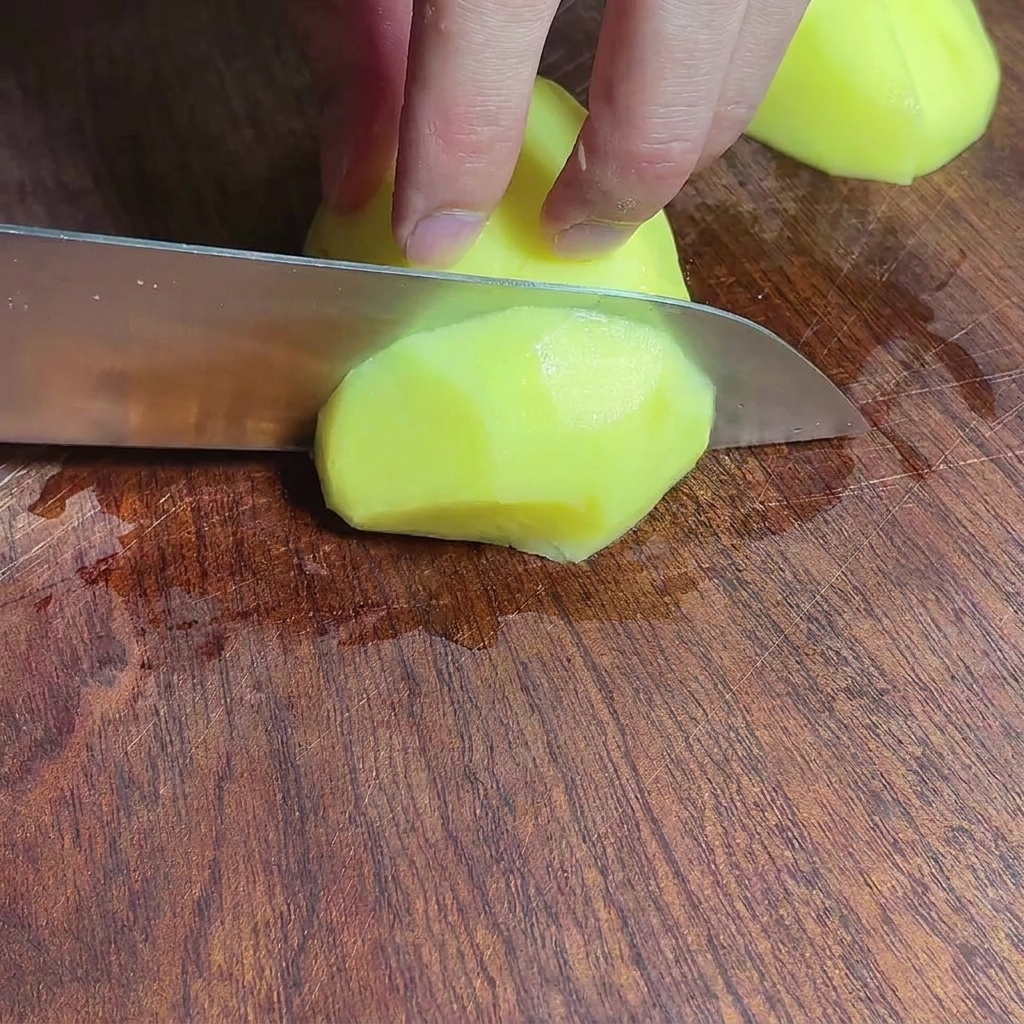 Chopped potato chunks on a wooden cutting board.