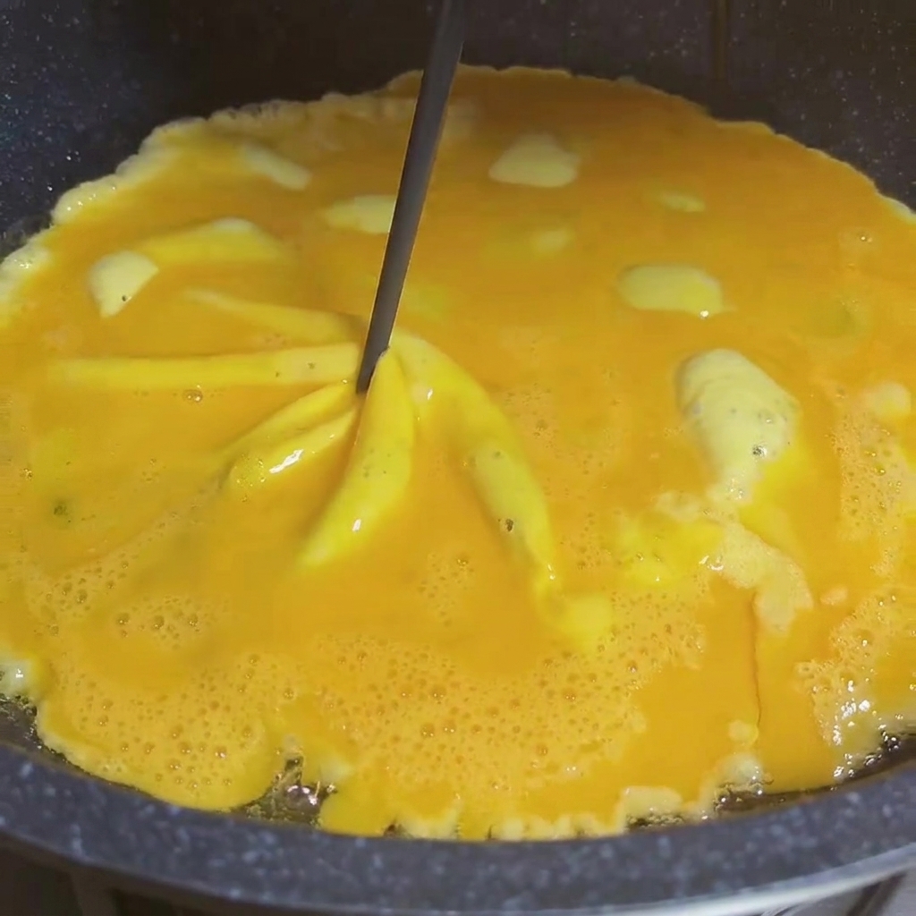 Close-up of two chopsticks swirling semi-cooked eggs in a pan to create a spiral whirlwind effect.