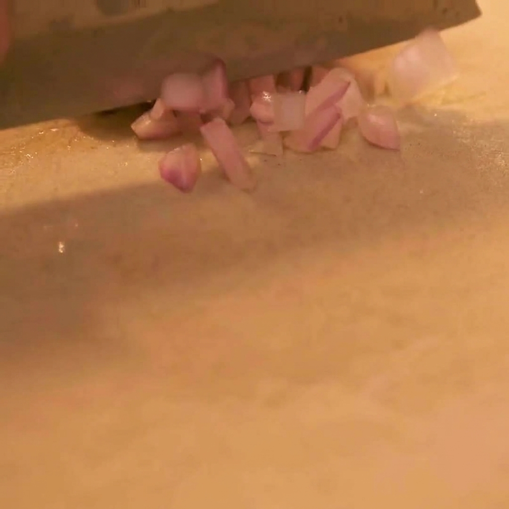 A close-up view of a sharp knife finely dicing a purple onion on a clean cutting board.