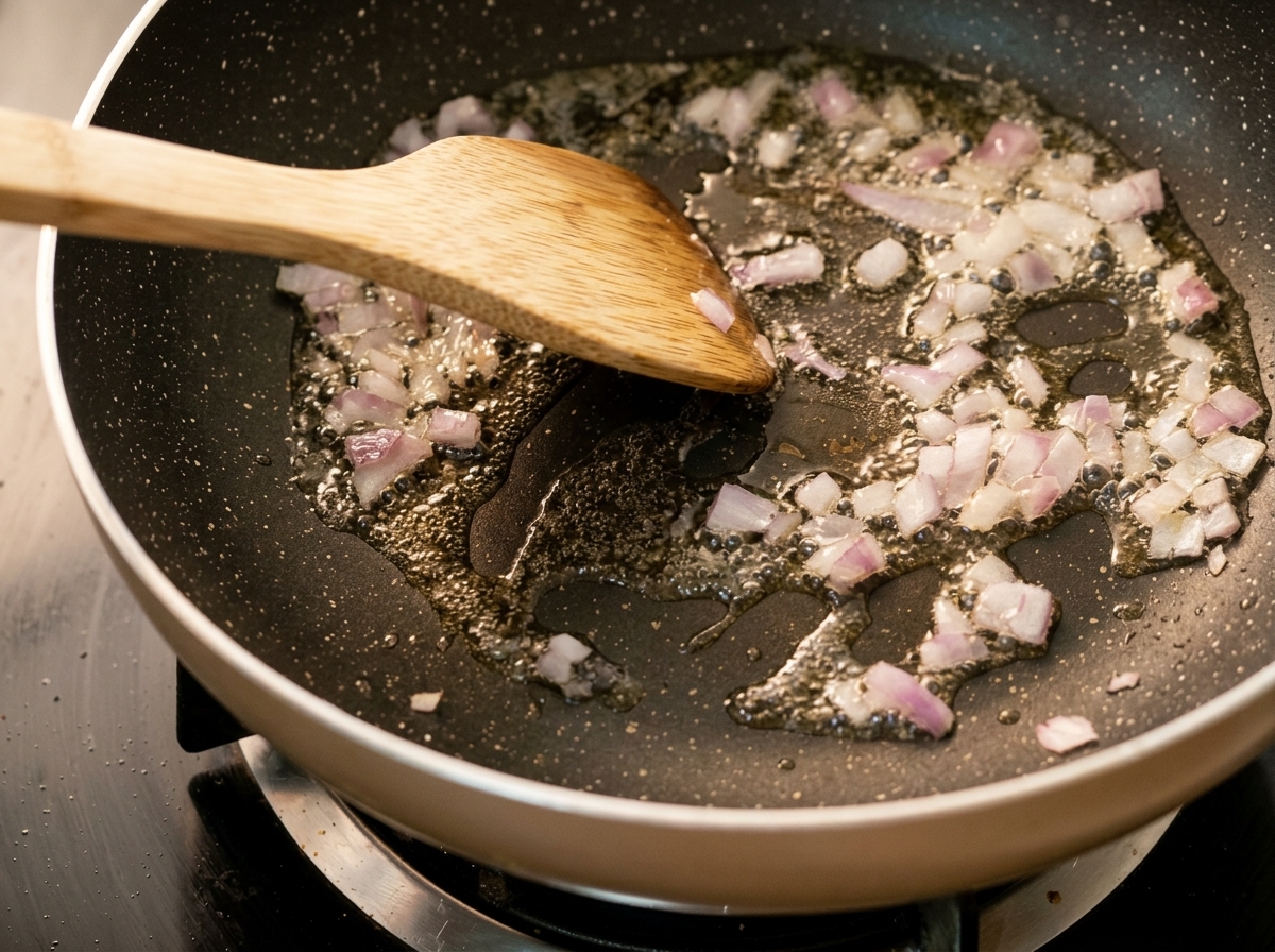 Minced onions cooking in a hot pan with oil, being stirred with a wooden spatula.