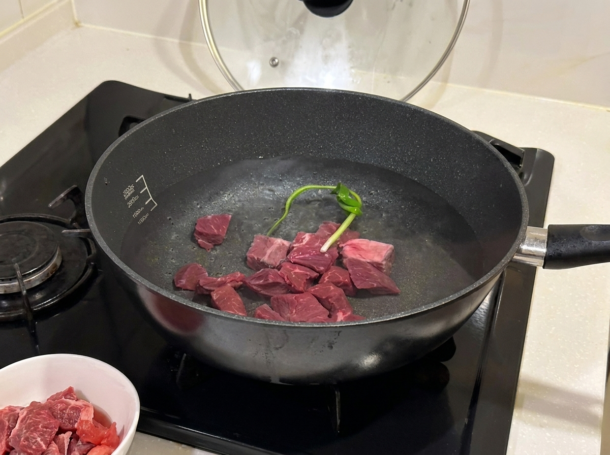 Beef chunks simmering in a pot with aromatics and cooking wine.