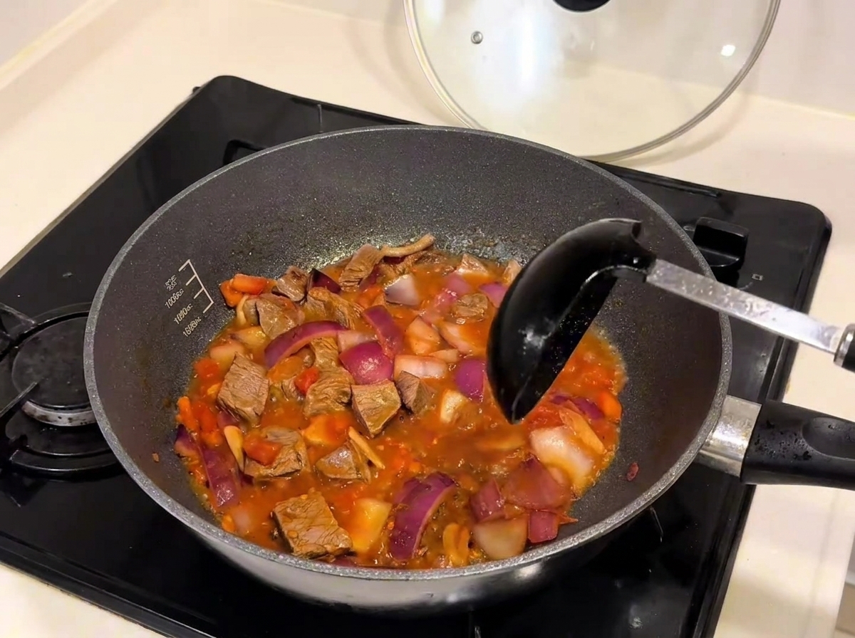 Hot water being poured from a kettle into a pan filled with beef and vegetables.