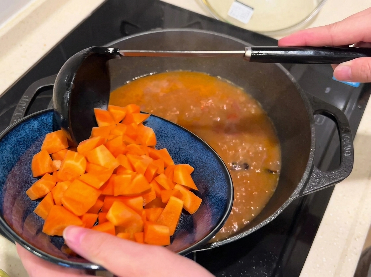 Diced carrots being added into a pan of simmering beef broth.