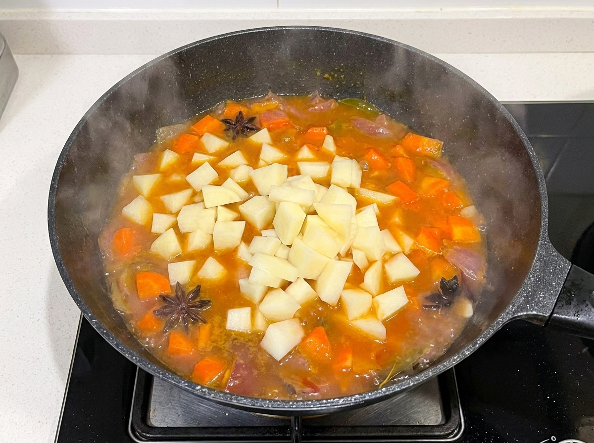 Diced potatoes being added into a pan containing boiling beef, carrot, and onion broth.