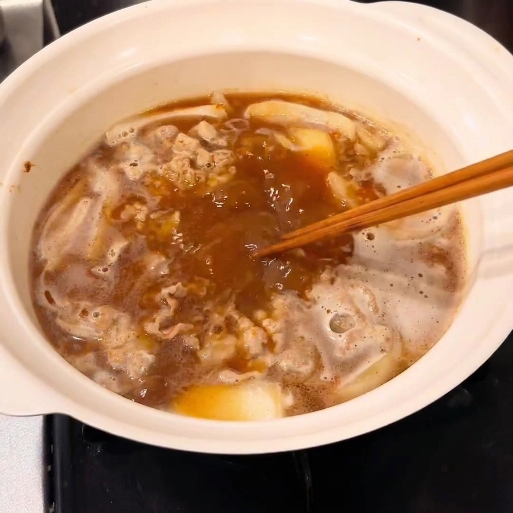 A block of curry roux being stirred into the pot to create a thickened sauce.