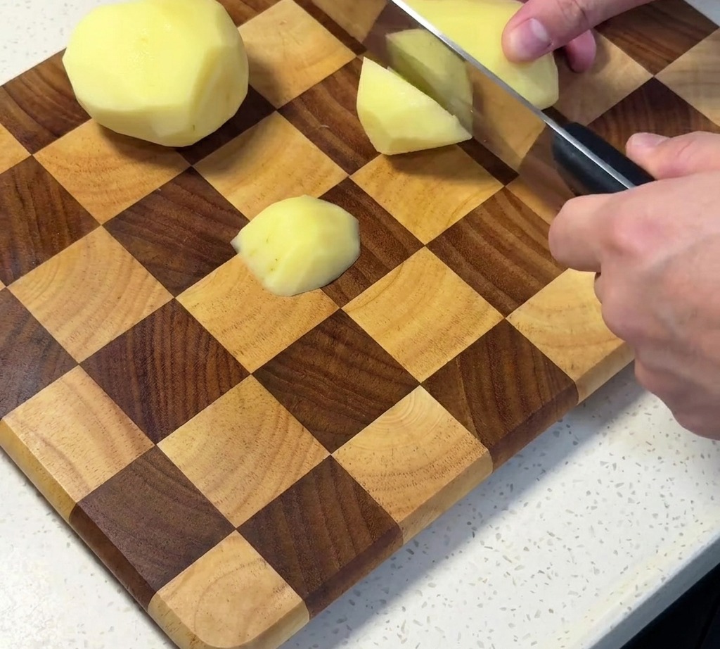 Peeled raw potatoes being diced into cubes on a wooden cutting board.