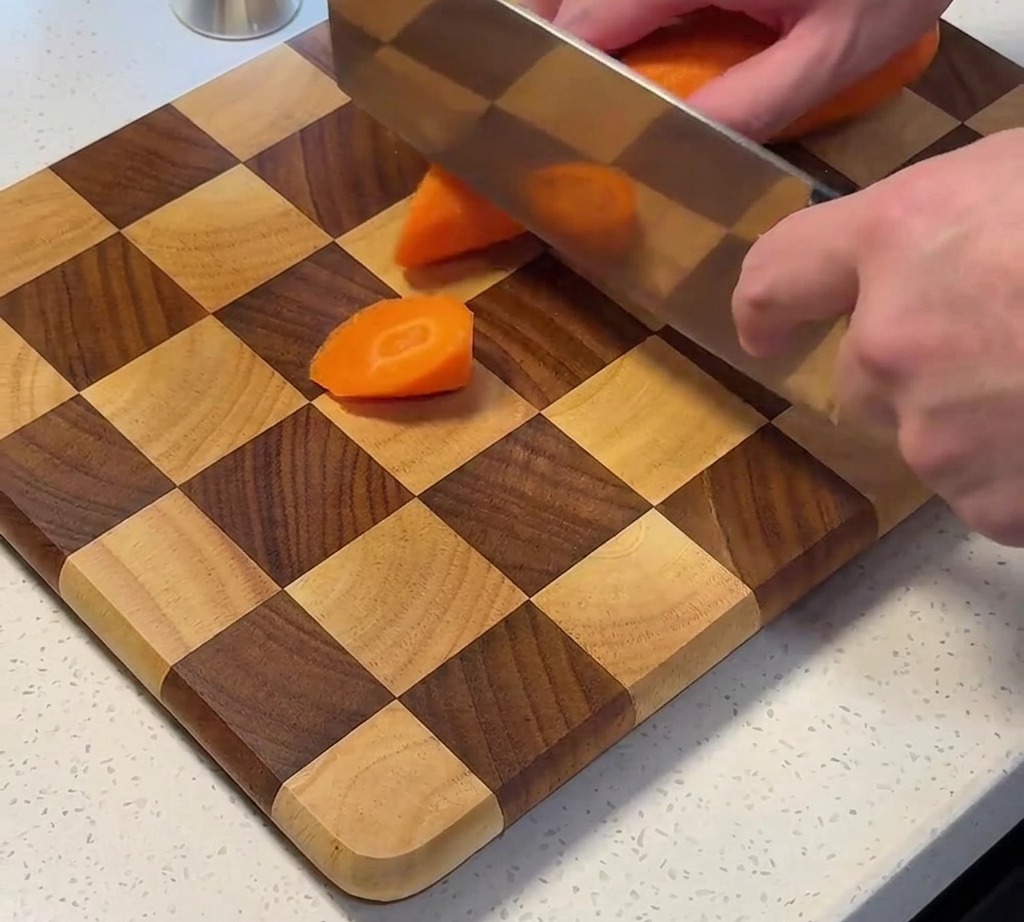 Fresh carrots being sliced into chunks on a wooden cutting board.