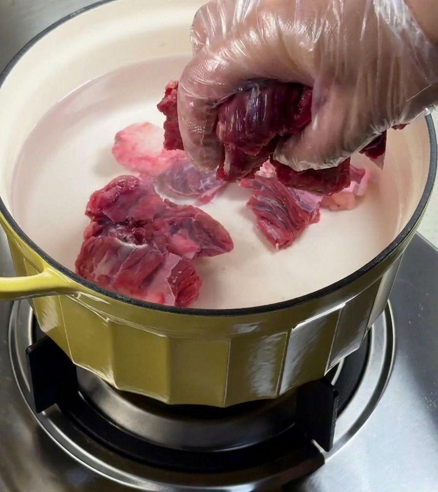Beef brisket being blanched in a pot of water with aromatics.