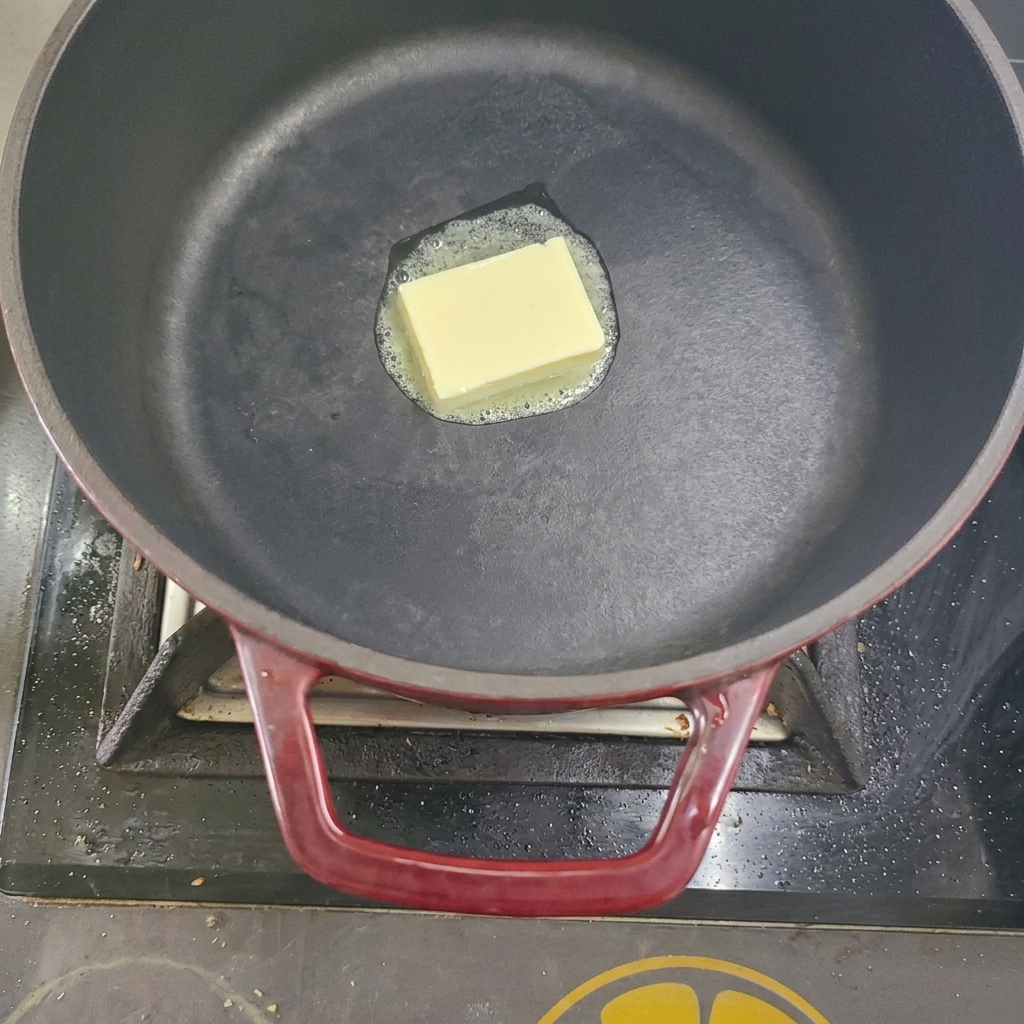 A cube of butter melting in a black pot on a stovetop.