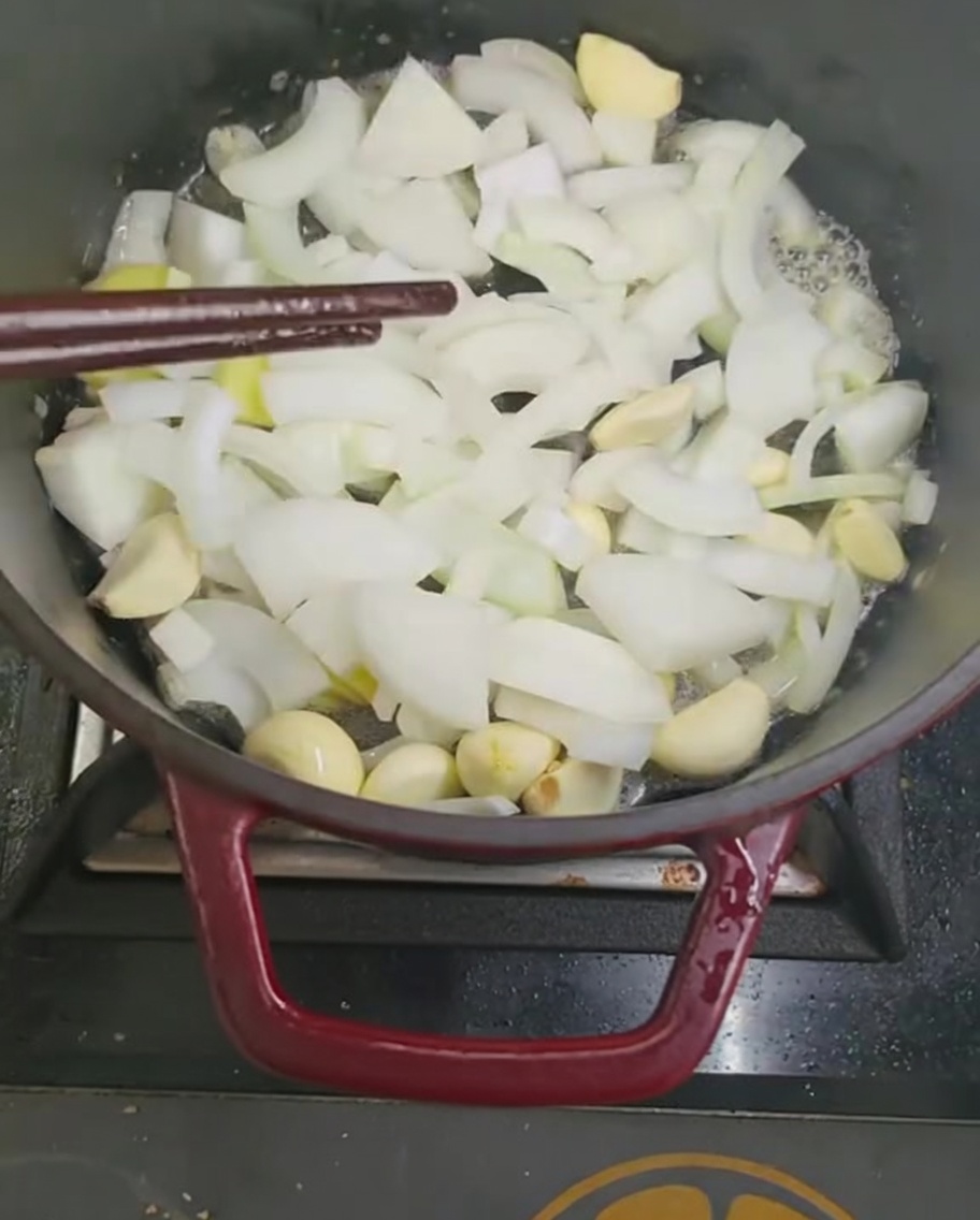 Sautéing onion and garlic pieces in a pot with chopsticks.