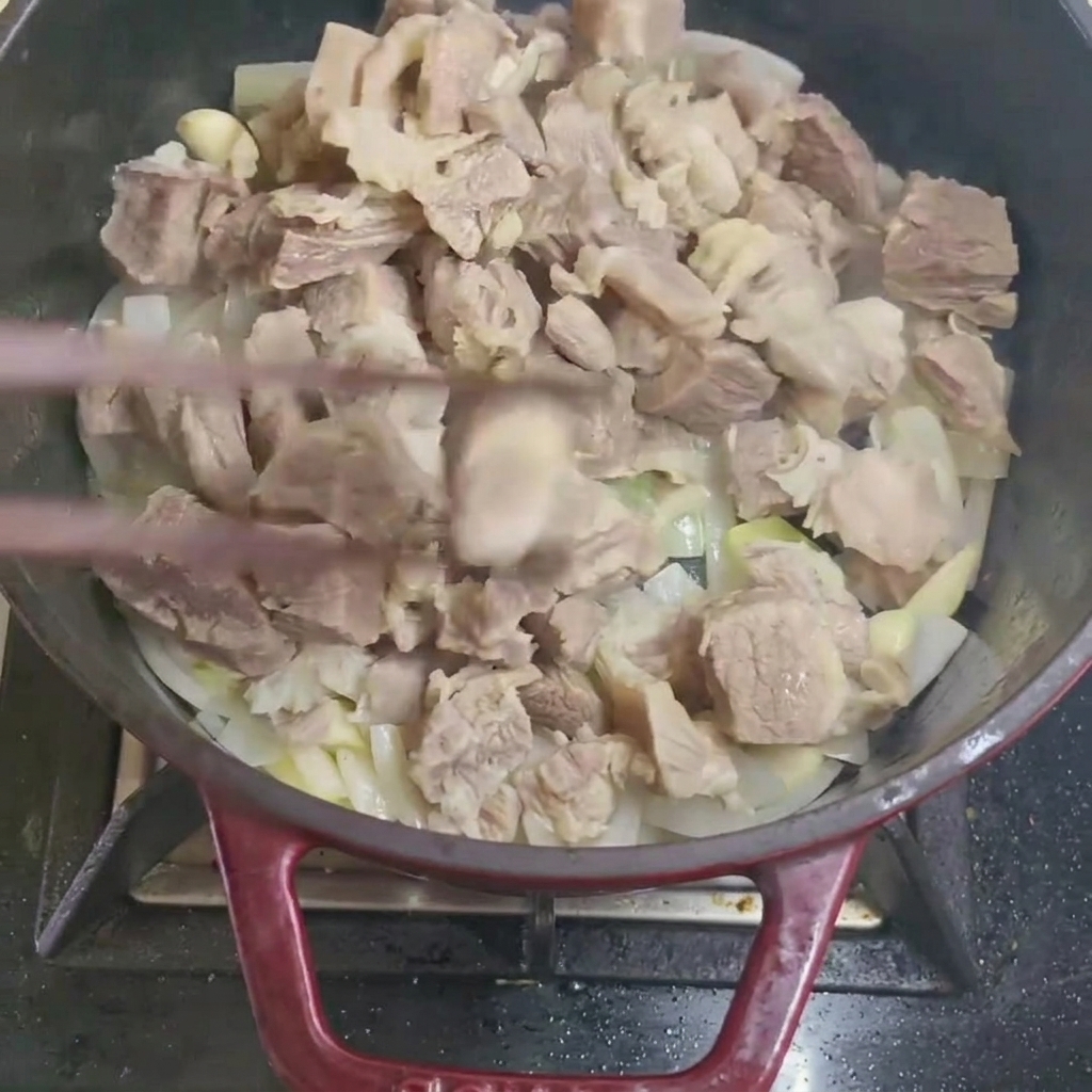 Stirring blanched beef chunks with onions and garlic in a pan.