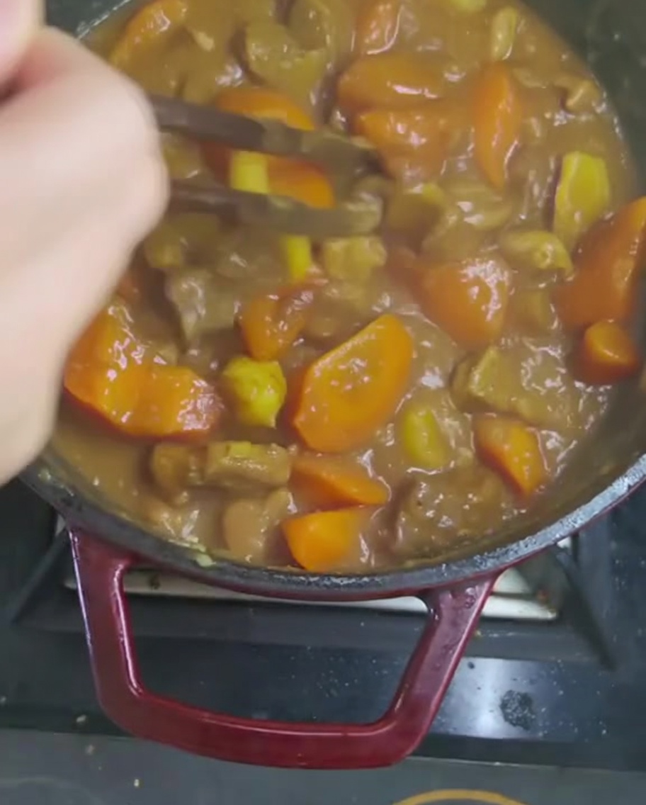 Stirring the thick curry sauce with a wooden utensil to fully dissolve the curry cubes.