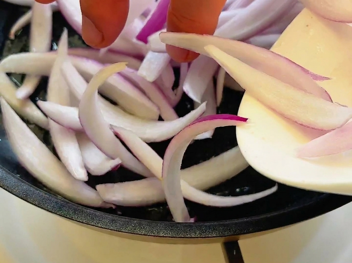 Red onion slices being sautéed in a skillet, turning translucent.